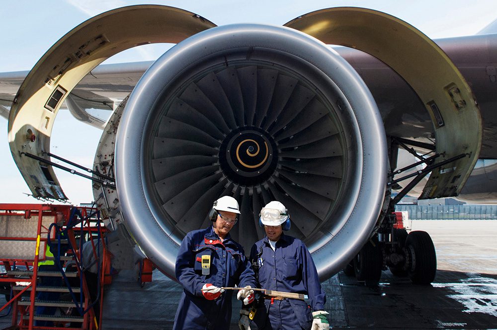 Two airplane mechanics in front of a jumbo jet engine.