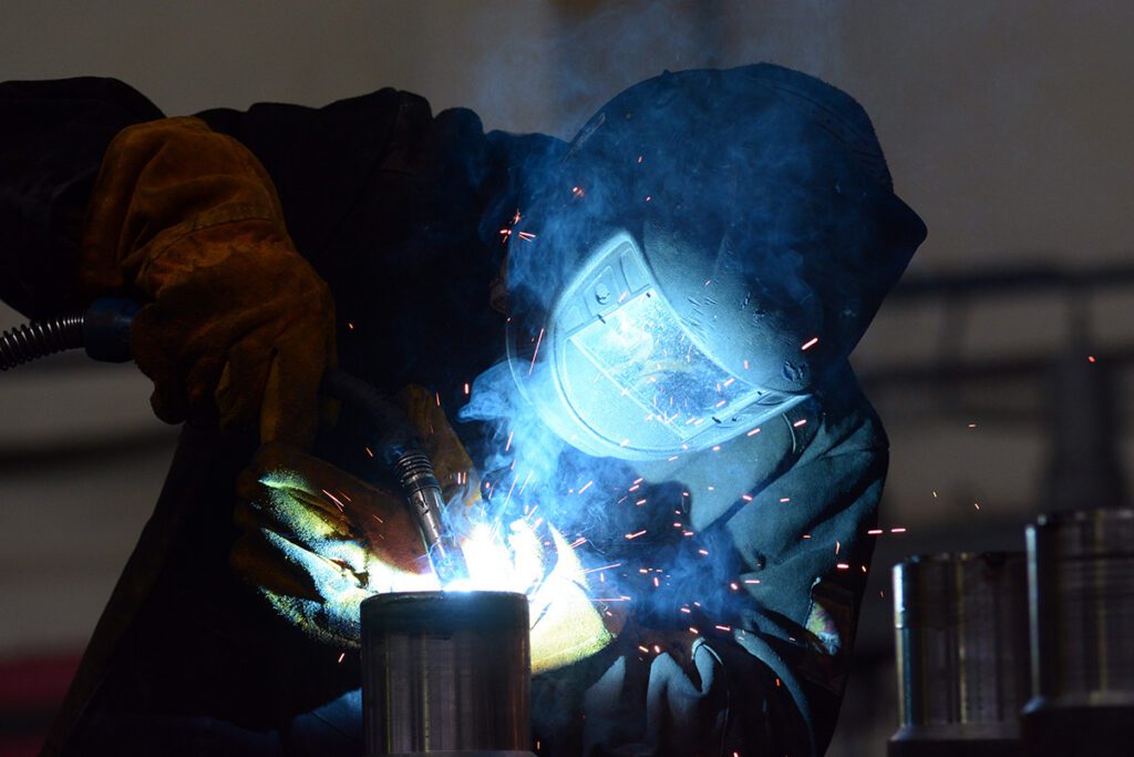 A person brazing two metals together with blue light emitting from the work.